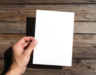 Obraz premium Hand Holding Blank White Paper on Rustic Wooden Table for Mockup and Design