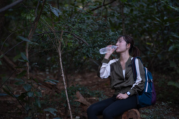 A woman is sitting on a log in the woods and drinking water