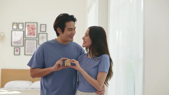 Asian Couple Holding Miniature House Model for Real Estate Investment.This image symbolizes home ownership, real estate investment, future planning, mortgage, family dreams, buying new house together.
