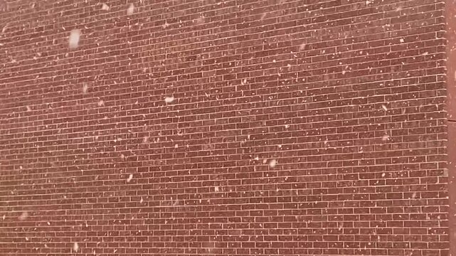 Snow falling against a red bricked apartment building