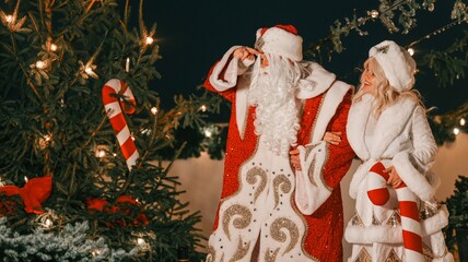 Father Frost and Snow Maiden pose by a Christmas tree with candy canes and lights