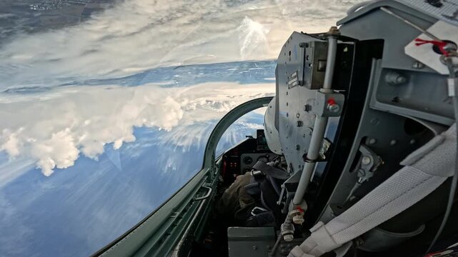 Upside down view from the military fighter jet cockpit performing maneuver, extreme aerobatic flight high in the blue sky above the white fluffy clouds