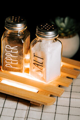 Salt and pepper shakers placed on a wooden stand with a plant in the background
