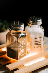 Salt and pepper shakers placed on a wooden tray with soft lighting in a cozy setting
