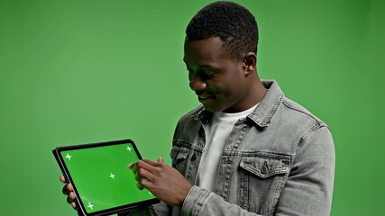 Man presents tablet on green screen during studio shoot.