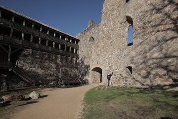 Fototapeta premium Ancient medieval castle courtyard with historic stone fortress walls and a multi-tiered wooden defensive gallery structure under a clear blue sky.
