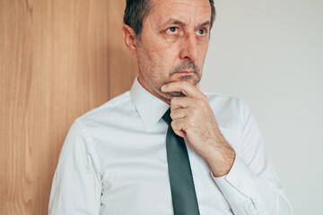 Thoughtful professional in formal attire resting hand on chin, contemplating strategy and business choices.