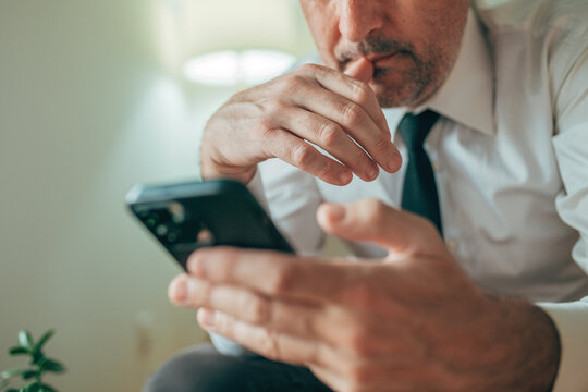 Pensive adult man using smartphone at home, close-up focus on hands and expression.