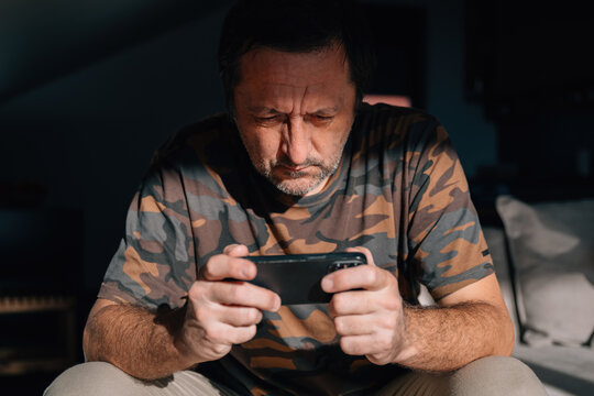 Close-up of a middle-aged man studying his phone with a tense, concentrated look, lit by strong natural light.