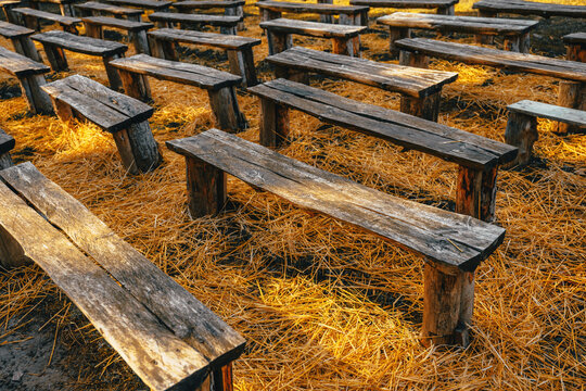 Old handmade wooden seating benches placed on hay in countryside environment, warm light and natural texture, rustic outdoor gathering spot.