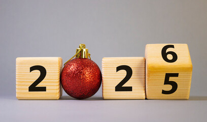 2026 New Year symbol. Businessman turns wooden cube and changes Year 2025 to 2026. Beautiful grey background with Christmas ball. Copy space. Business and 2026 happy new year concept