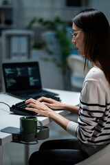 Focused Asian programmer wearing glasses, typing on a keyboard at late night in the office....