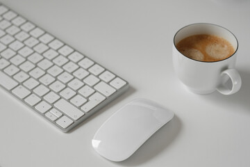 A minimalistic workplace with a white mongrel keyboard, mouse and a cup of hot coffee. Ideal for illustrating the topics of freelancing, productivity, morning, hard work, modern office.