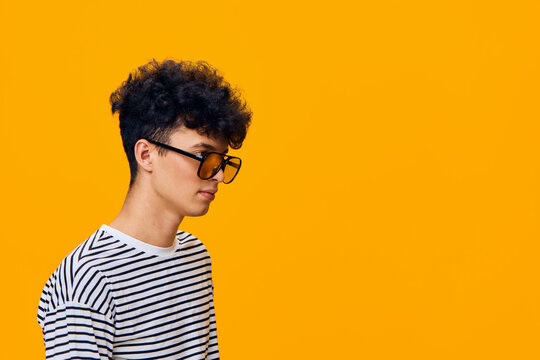 young man with glasses wearing striped shirt stands against vibrant yellow background with thoughtful expression and casual hairstyle - Powered by Adobe