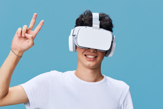 young man wearing virtual reality headset smiling and showing peace sign with hand against blue background, casual clothing, technology experience - Powered by Adobe