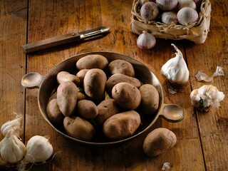 Freshly harvested potatoes and whole garlic cloves are arranged on a wooden table, ready to be transformed into a comforting Romanian dish for the winter season