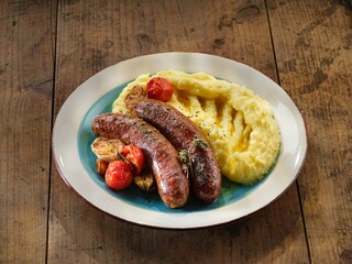 This hearty dish features succulent pork sausages accompanied by creamy mashed potatoes and beautifully roasted cherry tomatoes, perfect for a comforting meal