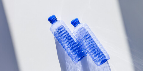 Blue plastic bottles at sunlight shadow on blue white background, top view empty plastic bottle for...