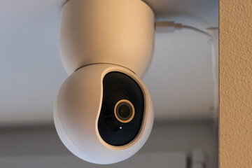 Modern white smart home security camera mounted on ceiling for indoor video surveillance and safety monitoring