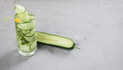 A clear glass of detox water, adorned with cucumber ribbons and mint leaves, sits against a gray cement background. © nndanko
