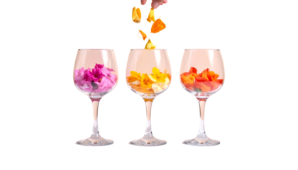 Three wine glasses fill with vibrant flowers, a hand pouring blooms. Black background