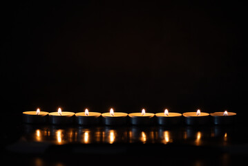A row of glowing tealight candles against a dark background. Perfect for themes of remembrance, meditation, spirituality, mourning, tranquility, or holiday celebrations.