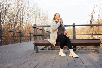 Casual middle-aged woman enjoys a coffee break while walking in park.