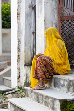 Indian woman dressed in yellow sari sitting at the house entrance
