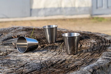 Fototapeta premium Three metal shot glasses on weathered tree stump, an essential accessory for men enjoying spirits during camping, hunting, or fishing trips.