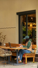 Woman working on laptop at outdoor cafe with dog on leash