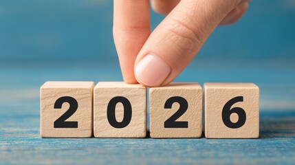 Hand placing a wooden block to complete the year 2026, representing future planning and goals