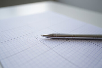 Close Up of Silver Pen on Grid Paper with Precise Lines and Geometric Pattern for Technical Drawing or Design Work on White Surface