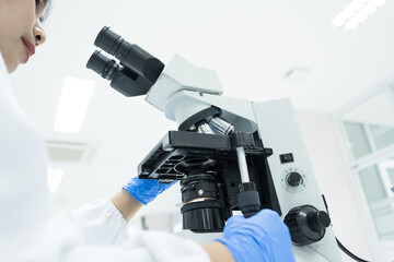 Selective focus woman Asian scientist using microscope to analyze blood smear slide sample at labolatory room.Specialist development and production of new medicines.