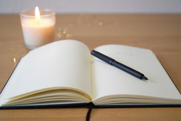 Open Journal with Blank Pages and Black Pen Next to Lit Candle on Wooden Desk for Mindfulness Practice and Personal Reflection 150 Char