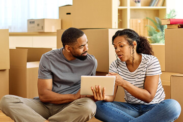 Portrait of a young couple unpacking, moving in and relocation to a new apartment, happy young couple  using a tablet, browsing and shopping online, , family new beginning sitting on the floor