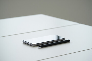Smartphone and Stylus Lying on White Surface Seen Up Close With Grey Background in Gentle Studio Lighting Offering Clean Business Mockup
