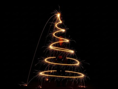 Christmas tree shape drawn with light painting using a sparkler against a dark black background for a festive holiday celebration