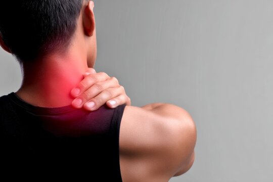 A young person holds their neck in discomfort. The image portrays tension and pain in the upper back area. This stock photo is useful for health-related topics and wellness content. AI