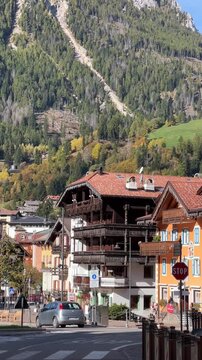 Moena, Italy - October 10, 2025: A charming street scene in Moena with traditional Alpine-style buildings, colorful facades and a backdrop of lush forests and towering mountains in the Dolomites.