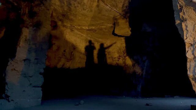 Two people&rsquo;s shadow silhouettes on ancient stone walls inside Fabrika Hill Cave Complex, one person raising a hand as if pointing at something, creating a dramatic and mysterious underground atmospher
