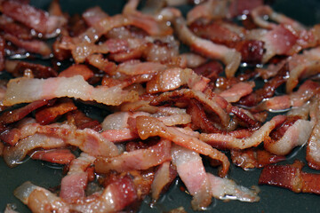 Sizzling bacon lardons frying in a pan close up