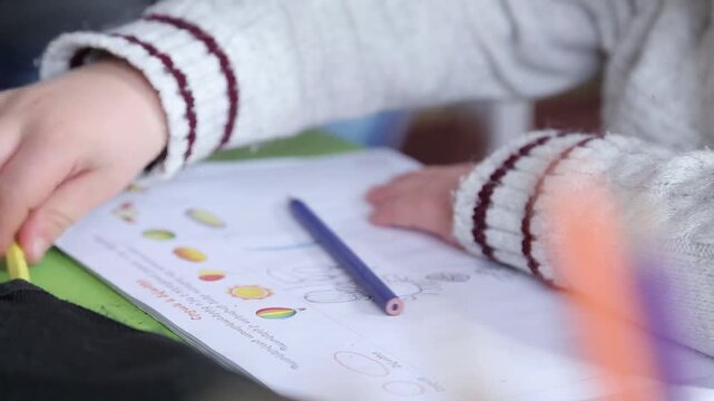 Close up shots of children's hands drawing and coloring. One kid colors a worksheet with a blue pencil, while a girl draws on white paper with a wooden pencil.

