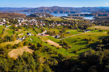 Wide aerial panorama of Polańczyk village and the Solina Lake (Jezioro Solińskie) in Bieszczady, Poland. Scenic October landscape with dam structure in the background.