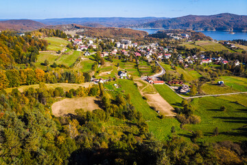Wide aerial panorama of Polańczyk village and the Solina Lake (Jezioro Solińskie) in Bieszczady, Poland. Scenic October landscape with dam structure in the background.