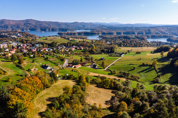 Wide aerial panorama of Polańczyk village and the Solina Lake (Jezioro Solińskie) in Bieszczady, Poland. Scenic October landscape with dam structure in the background.