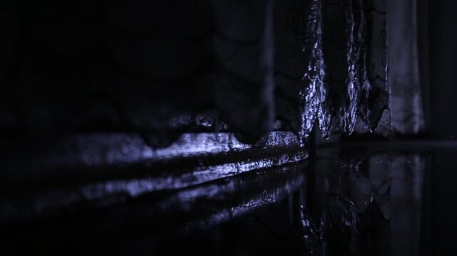 Heavy rain pouring down on a balcony floor at night. The dark scene shows water splashing and reflecting light on the wet surface, creating a moody atmosphere.


