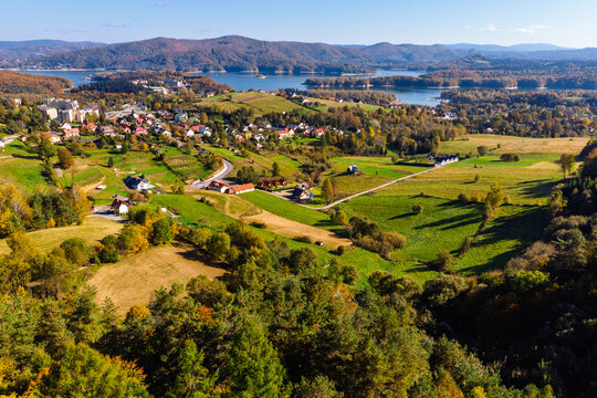 Wide aerial panorama of Polańczyk village and the Solina Lake (Jezioro Solińskie) in Bieszczady, Poland. Scenic October landscape with dam structure in the background.