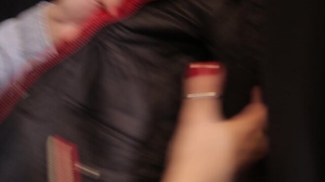 Close-up of female hands with red manicure opening the zipper of a black leather jacket pocket and taking out a bunch of keys with colorful keychains inside.

