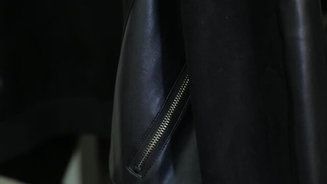 Close-up of female hands with red manicure opening the zipper of a black leather jacket pocket and taking out a bunch of keys with colorful keychains inside.

