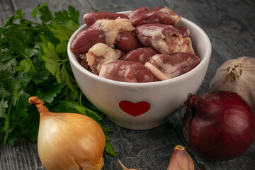 Raw Chicken Hearts in Bowl with Fresh Vegetables and Herbs on Rustic Wooden Table